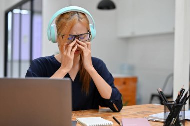 Kablosuz kulaklık takan üzgün genç bir kadın çalışma alanında otururken akıllı telefondan müzik dinliyor. Üzgün, başarısız, bunalımlı.