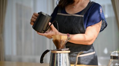 Kesilmiş resim, Asyalı yaşlı ya da emekli bir kadın kocasına oturma odasında sabah kahvesi hazırlıyor. Kahve ısıtıcısı, kahve yapmak..