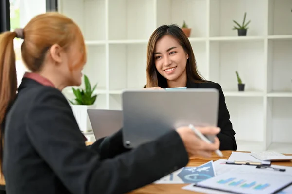 親切かつ肯定的なアジアの女性の上司は彼女の女性スタッフを聞いてオフィスのデジタルタブレットを介して新しいプロジェクトの詳細を提示 — ストック写真