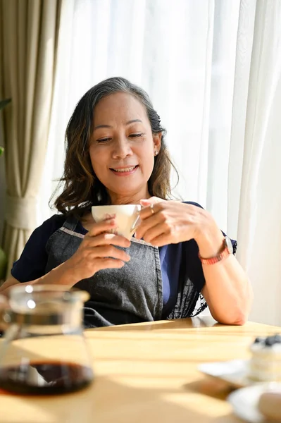 Portrait of a happy asian retired woman enjoy with her morning coffee in the house. Aged woman drinking and sipping hot coffee or tea.