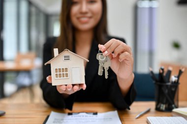 Emlakçı bir kadın emlakçı ev modeli ve hortum anahtarlarını tutuyor ya da gösteriyor. kırpılmış resim