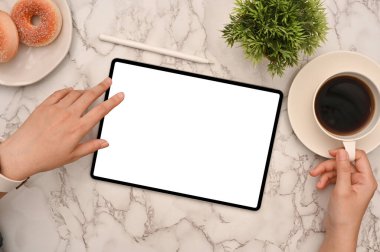 Üst görüntü, yakın çekim modern mermer masa çalışma alanında kahve içerken taşınabilir dijital tablet kullanan bir kadın. Boş tablet ekran modeli. 