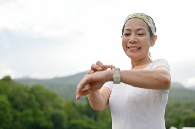 Mutlu Asyalı yaşlı kadın dışarıda egzersiz yapmayı seviyor. Yeşillik parkında koştuktan sonra kalp atışlarını kontrol ediyor. Spor ve teknoloji kavramı.
