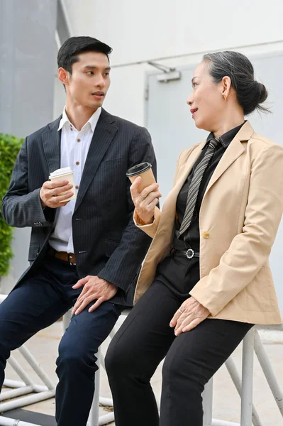 Neşeli Asyalı iş adamlarının portresi konuşuyor, kahve içiyor, öğle arasında binanın dışında dinleniyor..