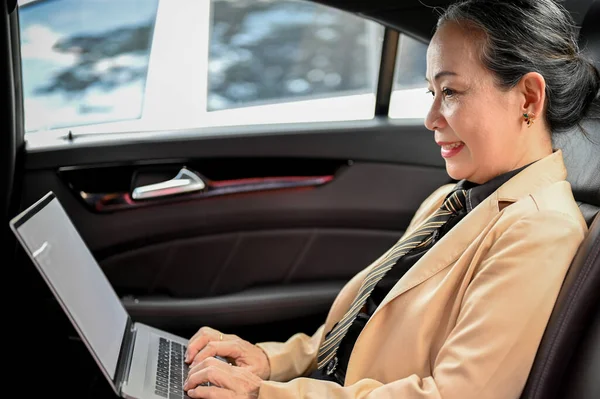 Successful aged asian businesswoman using portable laptop computer, working in the car during a rush hour on the road. Urban busy lifestyles concept.