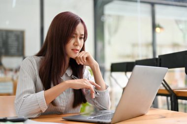 Asyalı mutsuz iş kadını dizüstü bilgisayar kullanıyor, şaşırmış ve proje sonuçlarından memnun değil..