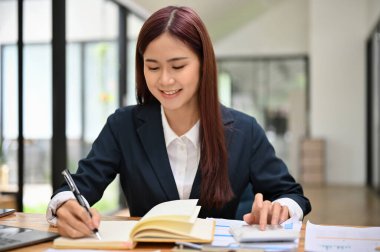 Muhasebe ödevi için çalışan bir kadın muhasebeci, ofis masasında iş vergisi ve fatura hesaplıyor..