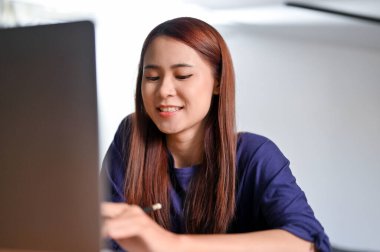 Güzel Asyalı genç kız üniversite öğrencisi dizüstü bilgisayar kullanıyor, online iş ödevini yapıyor, internette bir şeyler karıştırıyor..