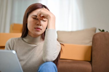 Stresli Asyalı genç bayan küçük işletme girişimcisi oturma odasında oturuyor, online satış siparişi konusunda ciddi..