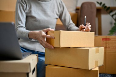 İnternetten alışveriş yapan kadın teslimat kutusu topluyor oturma odasındaki kutuya müşteri adresi yazıyor. kırpılmış resim