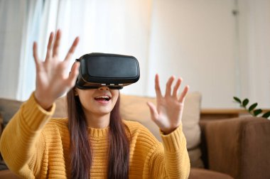 Çekici genç Asyalı kadın modern konforlu salonunda VR oyunu oynamaktan hoşlanıyor. VR kulaklık, Sanal gerçeklik oyunu deneyimi.