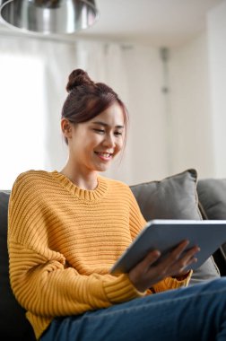 Çekici Asyalı genç bir kadının portresi oturma odasında rahat bir koltukta oturup en sevdiği filmi izlemek için taşınabilir tablet kullanıyor..