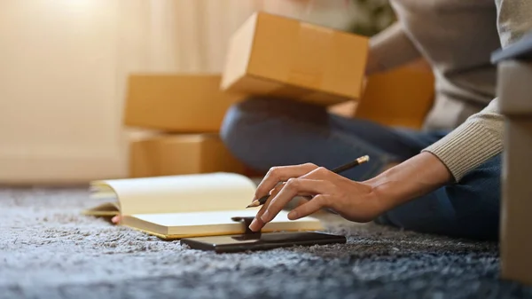 Female online shop owner packing her customer's order, checking the sending address on smartphone. Cropped, close-up image