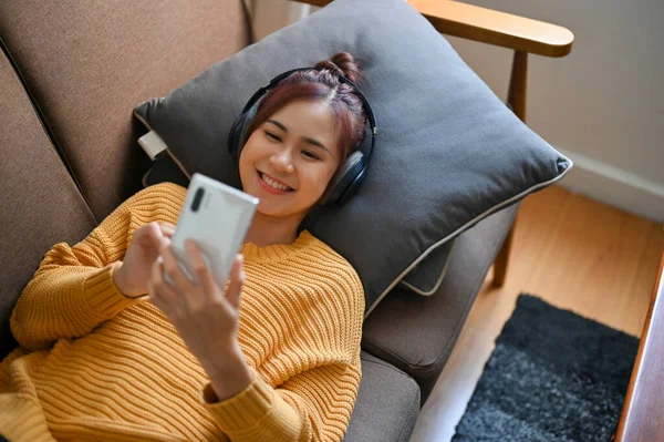 Щаслива Азіатка Лежить Зручному Дивані Користуючись Своїм Смартфоном Слухаючи Музику — стокове фото