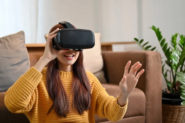 Modern oturma odasında VR gözlükleriyle sanal gerçeklik oyunu oynayan Asyalı heyecanlı bir kadın. VR oyun, VR kulaklık.