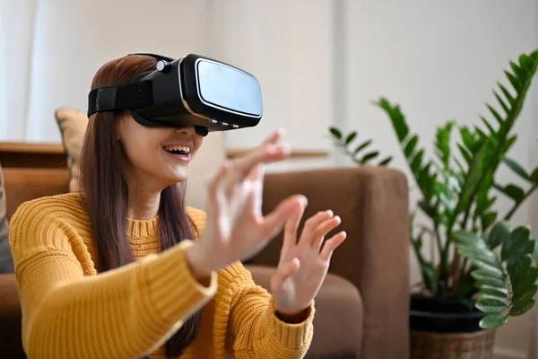 Milenyum Asyalı kadın oturma odasında video kayıt cihazı ile oyun oynuyor. VR oyunu oynayan heyecanlı bir kadın. Sanal teknoloji kavramı