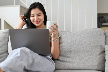 Güzel Asyalı kadın modern rahat oturma odasında dizüstü bilgisayarında film seyrediyor..