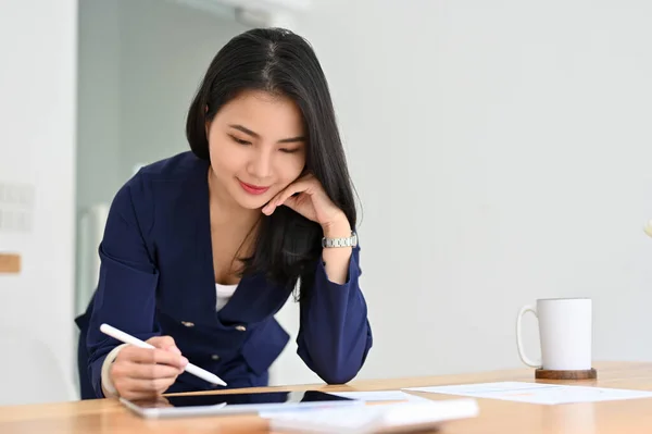 Gorgeous Asian businesswoman or female secretary working at her office desk, reviewing a business plan on tablet.