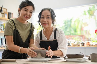 Güzel Asyalı yaşlı kadın, genç bir kadınla yaratıcı atölyede seramik tabak yaparak kilden zevk alıyor..