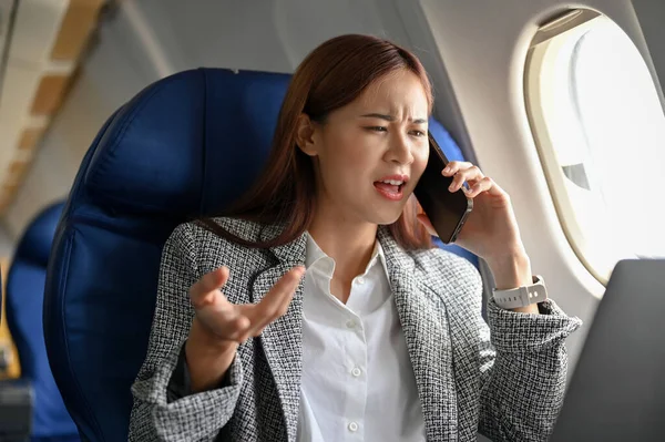 Angry mad asian businesswoman on the airplane, arguing and complaining problems on the phone to her boring secretary. Travelling and businesspeople concept.