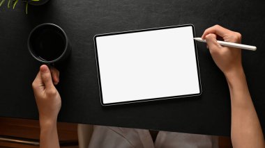 Üst Manzara, bir adam grafik tasarımcısı dijital tablet dokunmatik pedini stili kalemle tasarlıyor ve modern koyu ofis masasında sabah kahvesini yudumluyor..