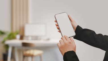 Bir iş kadını resmi bir takım elbise içinde arka planda bulanık beyaz ofis çalışma alanının üzerinde akıllı telefon beyaz ekran modeli tutuyor. 3d görüntüleme, 3d illüstrasyon