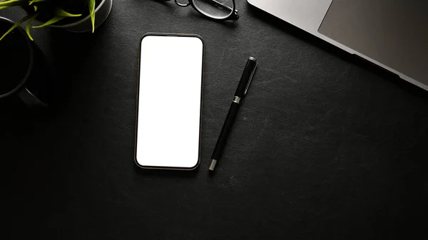 Minimal black workspace top view, flat lay with smartphone or cellphone white screen mockup, pen, laptop and decor.