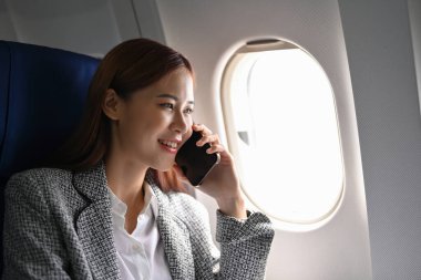 Başarılı ve kendinden emin resmi takım elbiseli Asyalı iş kadını iş ortağıyla telefonda konuşurken bir yandan da uçakla başka bir şehre iş gezisi yapıyor..
