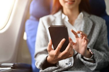 Yakın plan görüntü, başarılı bir Asyalı iş kadını ya da resmi takım elbiseli kadın girişimci birinci sınıf koltukta oturuyor ve uçuş sırasında akıllı telefon kullanıyor..