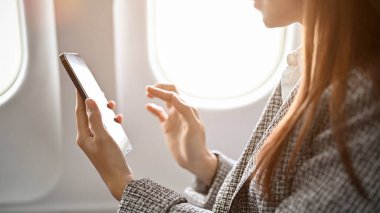 Asyalı iş kadını ya da kadın girişimci akıllı telefonu e-posta okumak ve başka bir şehre uçarken buluşma programını kontrol etmek için kullanıyor. kırpılmış resim