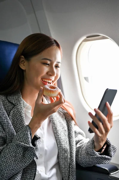 Relaxed Millennial Asian Businesswoman Eating Yummy Doughnut Using Smartphone While — Stock Photo, Image