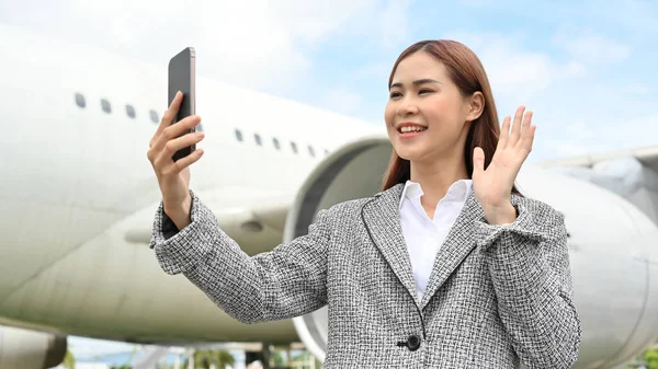 Beautiful and charming young asian businesswoman using a smartphone to video call with her family before going to another country by plane. Travelling, transportation concept.