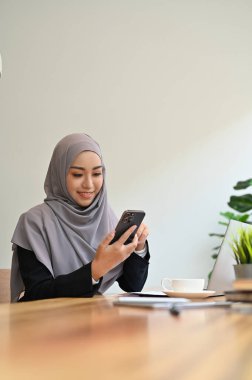 Güzel Müslüman iş kadını ya da kadın yönetici tesettüre oturuyor ve akıllı telefon kullanıyor..