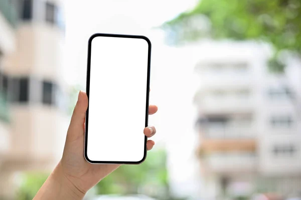 A smartphone white screen mockup in a female\'s hand over blurred flat or apartment building in the background. cropped image