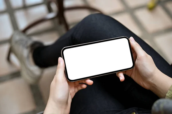 A female hands holding a smartphone in horizontal way, watching some video clip on the internet, playing mobile game. Phone blank screen mockup.
