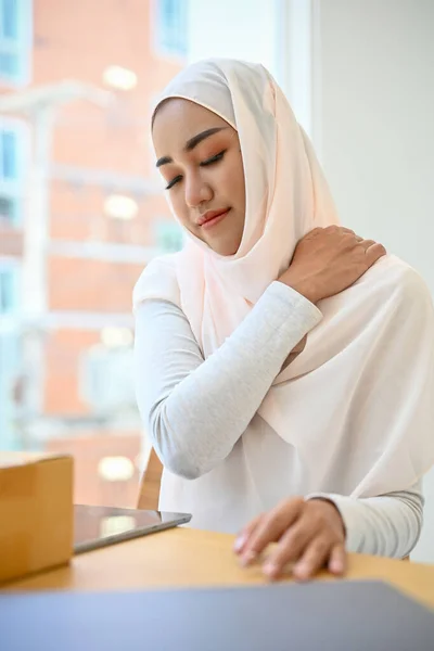 Tired young asian muslim businesswoman or female worker suffering from shoulder and back pain.