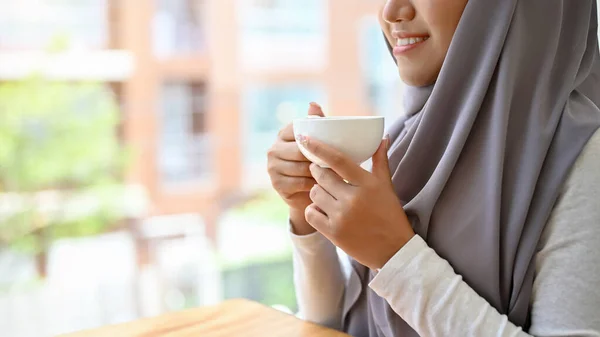 自宅やオフィスで朝のコーヒーを飲みながらヒジャーブのリラックスした美しい魅力的なイスラム教徒の女性 クロップドイメージコーヒーカップを持ち — ストック写真