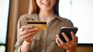 Yakın plan görüntü, elinde kredi kartı ve akıllı telefon olan güzel bir Asyalı kadın. Çevrimiçi alışveriş, çevrimiçi ödeme, internet bankacılığı kavramı