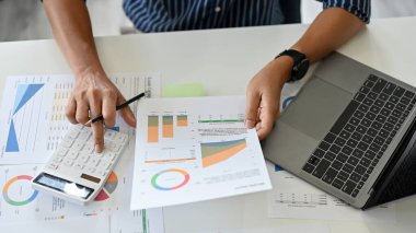 Masasında çalışan akıllı bir iş adamı, erkek muhasebeci ya da finans çalışanı mali raporları inceleyip hesap makinesi kullanıyor..
