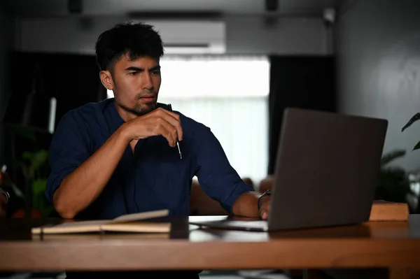 Stressed serious and professional Asian businessman or male tech engineer remote working at his home, using a laptop computer.