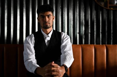 Yakışıklı, zeki ve başarılı Asyalı iş adamı veya resmi takım elbiseli patron portresi modern karanlık ofis odasındaki deri koltukta oturur..