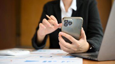 Ofis masasında akıllı telefon kullanan bir iş kadını ya da kadın finans müdürü. Görüntüyü kapat ve odakla.