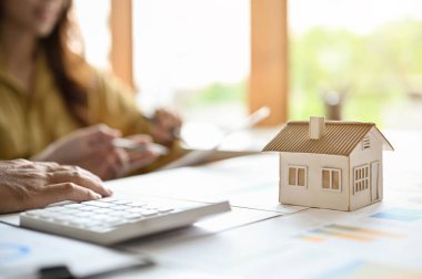 A female real estate agent or realtor having a meeting with client in the office. Close-up, selective focus image of a house model on the table.