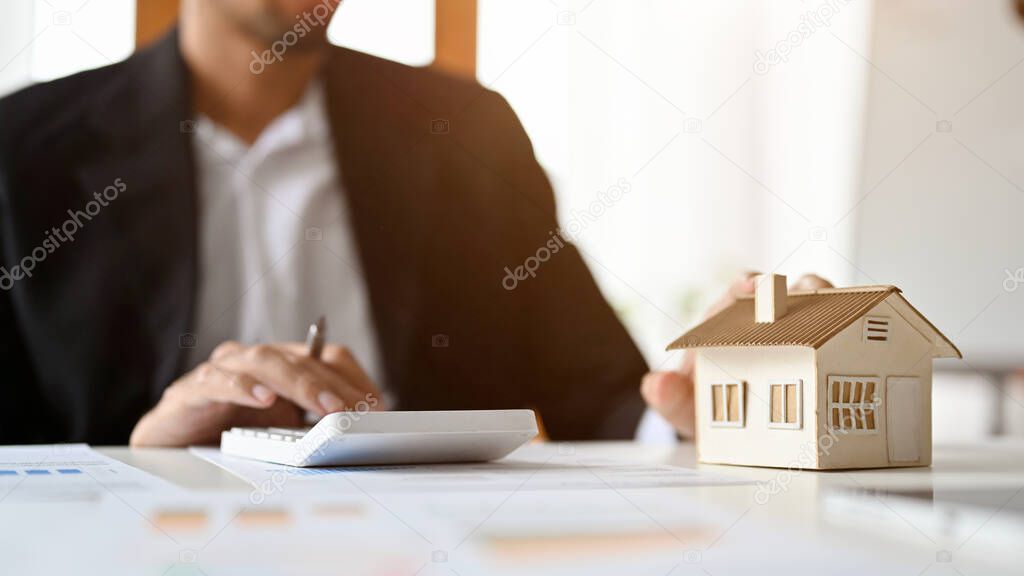 Cropped and selective focus, Professional male real estate agent or realtor using calculator, calculator rental tax at his office desk.