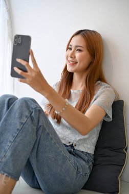 Milenyum Asyalı güzel bir kadının portresi selfie çekiyor ya da akıllı telefonuyla sosyal medyada canlı yayın yapıyor..