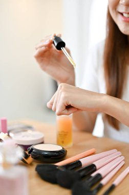 Kesilmiş ve yakından çekilmiş, yetenekli Asyalı genç bayan güzellik blogcusu elinde bir cilt serumu test ediyor, kozmetik ürününü inceliyor..