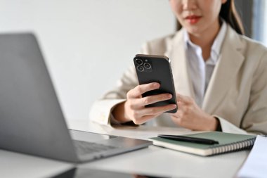 Güzel Asyalı kadın yönetici ya da iş kadını masasında internetten bilgi aramak için akıllı telefon kullanıyor. kırpılmış atış