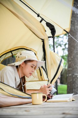 Çekici genç Asyalı kadın kamp çadırında uzanıp doğal ormanda kitap okuyor. arka plan, kamp faaliyeti kavramı.