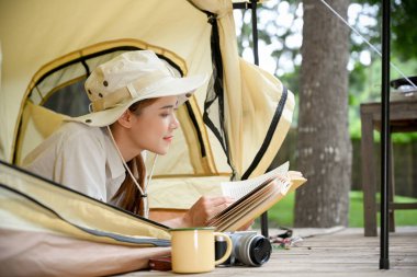 Çekici ve sakin genç Asyalı kadın kamp çadırında uzanıp kitap okuyor. arka plan, kamp faaliyeti kavramı.