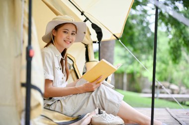 Güzel ve çekici Asyalı genç bayan kampçı çadırında en sevdiği kitapla oturuyor. Kamp kavramı